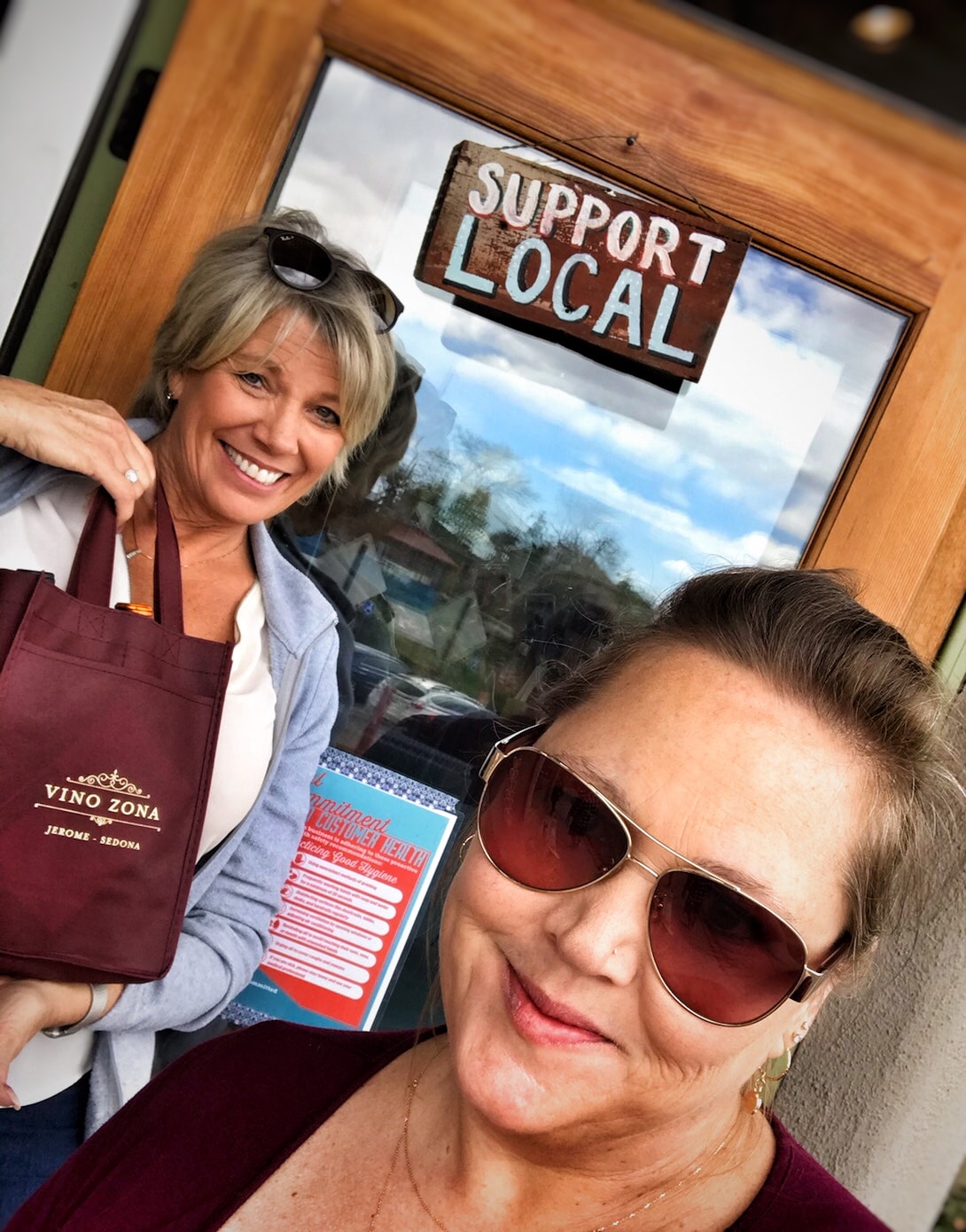 Two women with Vino Zona bag at Support Local sign